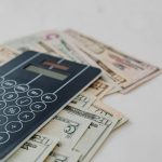 A close-up of a calculator and US dollar banknotes, symbolizing financial calculation and budgeting.